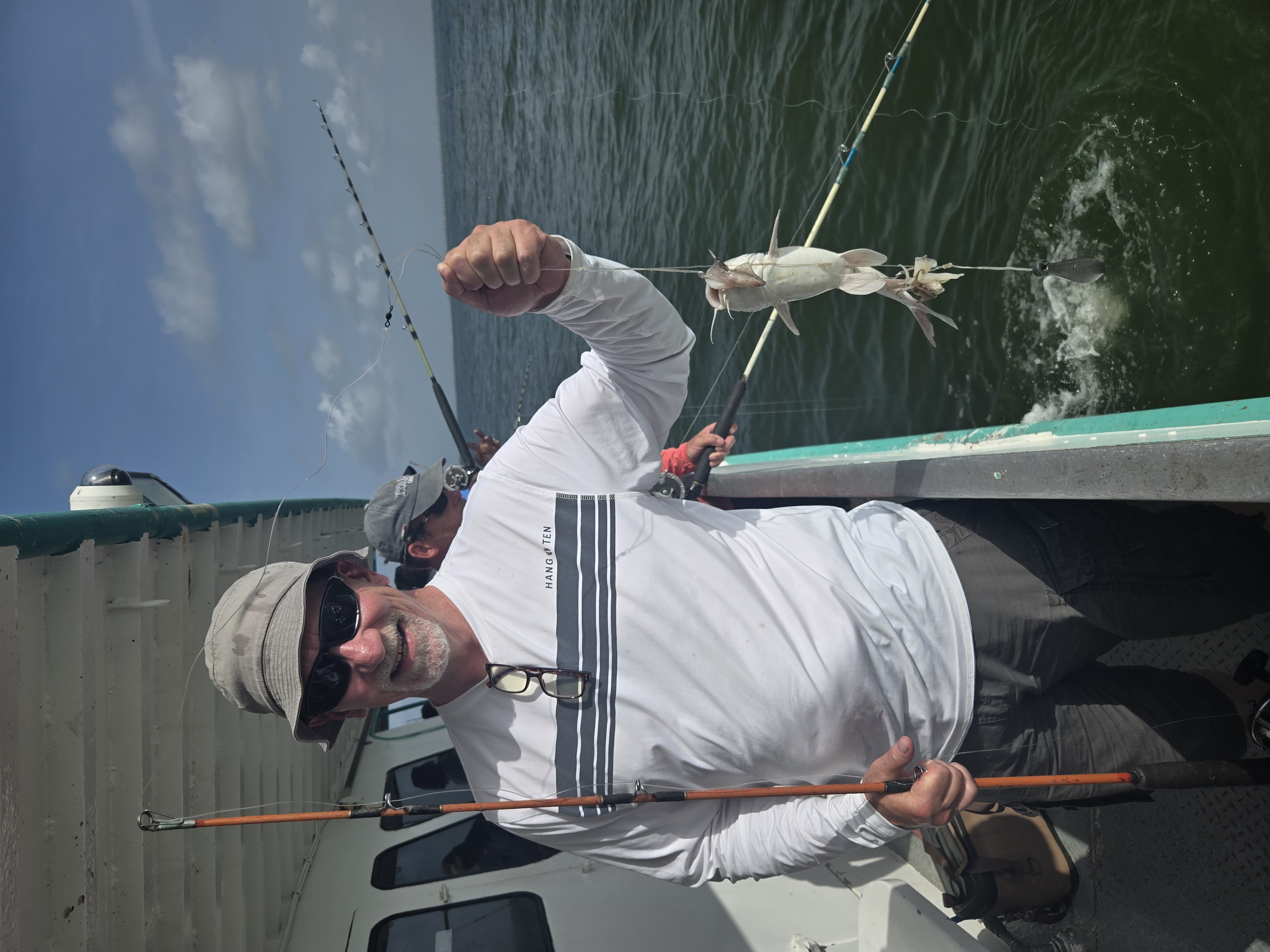 Dad smiling on a fishing boat, holding up a fish he just caught on the water